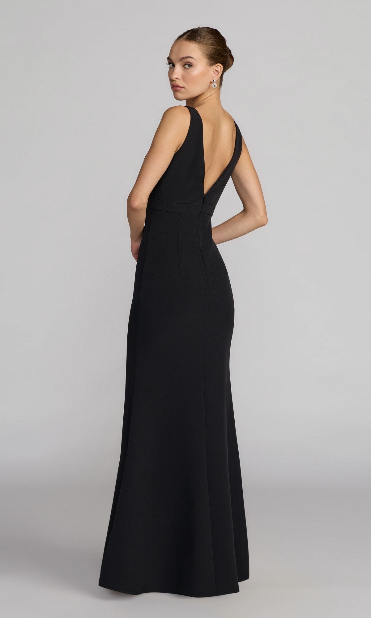 A woman models the Long Formal Dress: Mac Duggal 2371, a sleeveless black crepe evening gown with a deep V-back, shown against a plain light gray background.